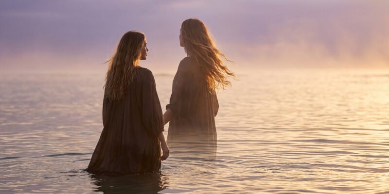 Why are Pisces so mysterious and hard to read — woman standing in shallow ocean water at dusk, soft mist around her, dreamy and ethereal mood